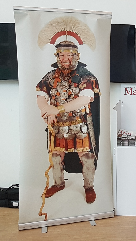 Moderne banner met daarop een foto van een van de leden van Corbulo in Romeins militaire outfit.